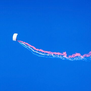 Parachutist Seen Against A Deep Blue Sky Trailing Multicolor Smoke