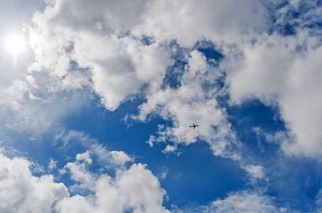 The sun is shining in a blue sky with white clouds, and the plane is flying