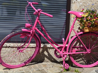 Pinkes Fahrrad mit Blumen im Korb vor einem Schaufenster