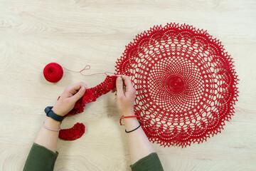 Hands of a craftswoman with a ball of red threads. Unusual hobby crochet. Background with copy space