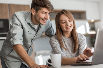 Fototapeta premium Cute couple using laptop together at home in the kitchen