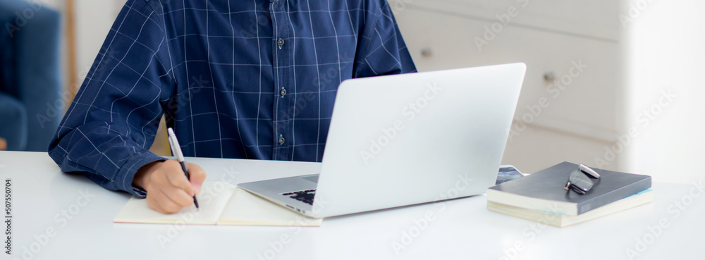 Wall mural Young asian business man in face mask for protect covid-19 and work on laptop computer and writing notebook, businessman quarantine work from home, new normal, social distancing and stay home.