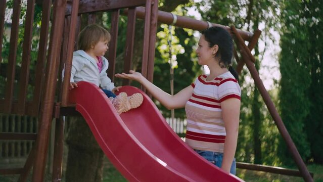 Mom helps her daughter get off the slide. Happy child playing with parents at home. The mother spends time with the child and has fun with her.