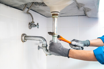 Technician plumber using a wrench to repair a water pipe under the sink. Concept of maintenance,...