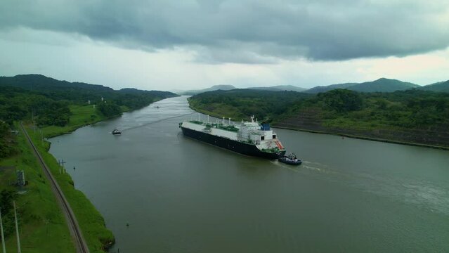 AERIAL: Massive freight ship is assisted along the breathtaking Panama channel by a smaller ship. Flying along the shores of Panama Canal as a large cargo ship gets assisted along the wide river.