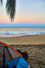 camping tent in front of the beach at sunrise with sky full of colors and palm tree in first plane on sayulita beach 