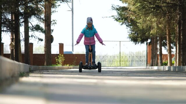 Closeup of little girl balancing on a hoverboard, learning to ride a gyro scooter outdoors. Personal eco transport concept