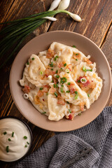 Potato dumplings with sour cream on the wooden table. Traditional ukrainian food. Varenyky, vareniki, pierogi, pyrohy - dumplings with filling.