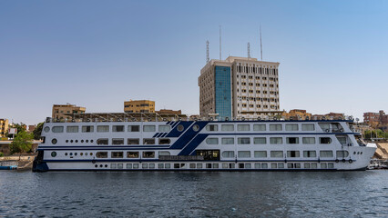 The cruise ship is moored at the river bank. Cabin windows are visible, lifebuoys on the upper...