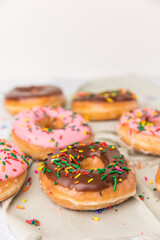 There are several strawberry and chocolate sprinkled donuts in different spots on a green napkin. 