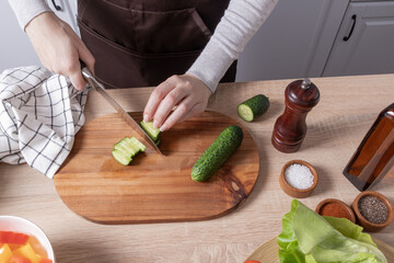 the hands of a young girl cut fresh cucumber for a salad on a cutting board and kitchen countertop.concept of cooking healthy food.