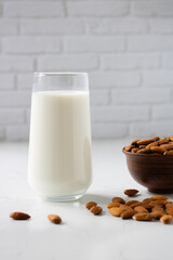 A glass of almond milk close-up next to a bowl with almonds and scattered almonds.