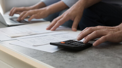 Close up hands of elderly family couple work with domestic financial papers use laptop calculator on cozy table at home office. Spouses retirees count household budget check receipts pay bills online