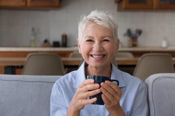 Cozy coffee break. Happy satisfied senior adult woman grandmother look at camera sit on comfortable...