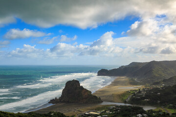 Obraz premium Piha, a coastal town west of Auckland, New Zealand. Lion Rock stands on the beach. In the background is Te Waha Point