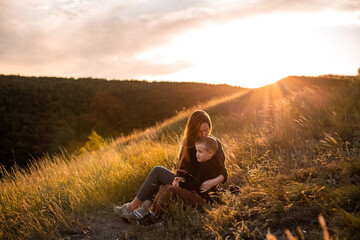 Mom and son walk in nature in the park at sunset along a country road. They sit and watch the sunset.