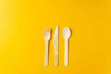 Disposable tableware from natural materials - bamboo wooden fork, spoon and knife isolated on a yellow background.