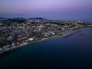 Fototapeta premium Aerial view of post-sunset glow over coastal town on point