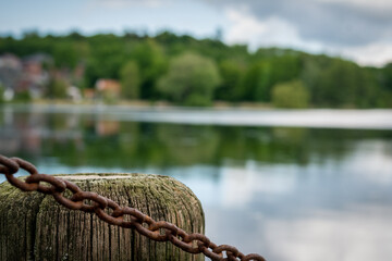 Poller aus Holz mit einer verrosteten Kette an einem See