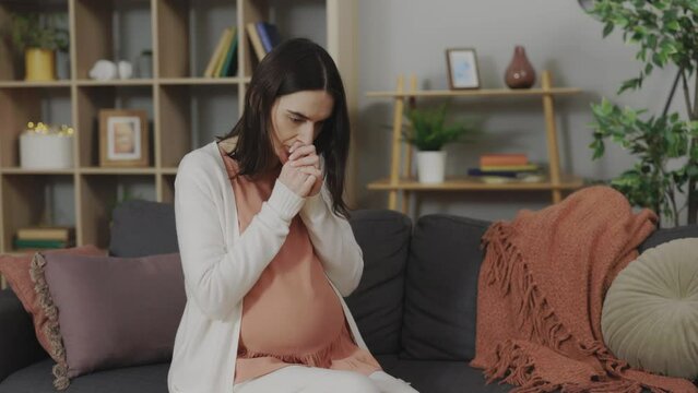 Caucasian pregnant woman feeling stress and anxiety while sitting alone on sofa. Young expectant mother thinking about upcoming birth of child.