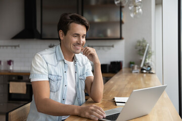 Obraz premium Happy self employed business professional working from home, using laptop, making video call, looking at screen. Male employee, adult student chatting online, watching virtual content, smiling