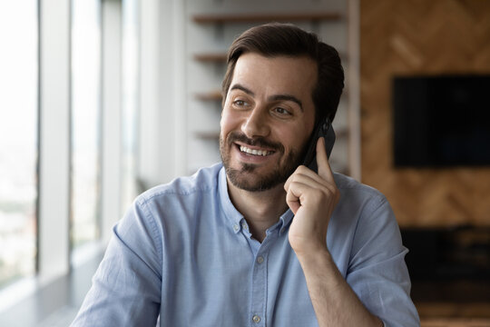 Happy millennial business man talking on mobile phone with toothy smile, making telephone call, consulting customer support service, looking away, thinking, getting good news, enjoying conversation