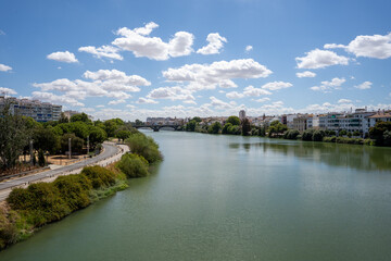 Naklejka na ściany i meble a large wide green river that flows through the Spanish city of Seville with green trees and white houses on both sides