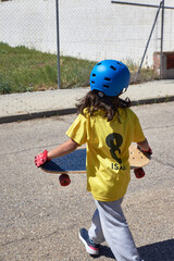 girl with her back turned walking down a street carrying a skateboard. On her T-shirt is inscribed the number 8 and her name: "Isabel".