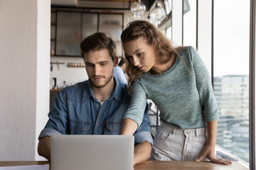 Corporate coach teaching new employee, training intern, explaining how to use work app on laptop, showing learning presentation. Business coworkers sharing computer, meeting at workplace, talking