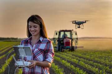 Farmer woman driving drone in field with tractor in background