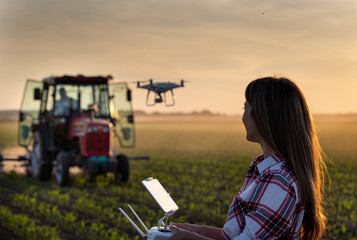 Bäuerin, die Drohne im Feld mit Traktor im Hintergrund fährt
