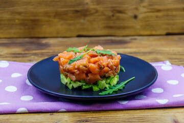 Salmon tartare with avocado and arugula on wooden table