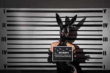 Sexy playboy girl in black latex suit at the background of mugshot ruler