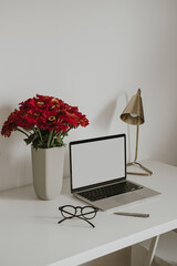 Laptop computer with blank copy space display on table with stationery, flowers bouquet, lamp....