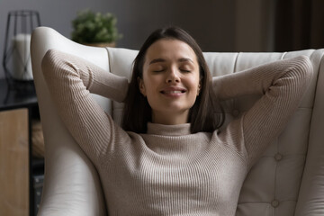 Happy peaceful satisfied pretty girl relaxing in soft comfortable armchair, leaning on back with closed eyes, smiling at good deep thoughts, enjoying relaxation, home leisure, breathing fresh air