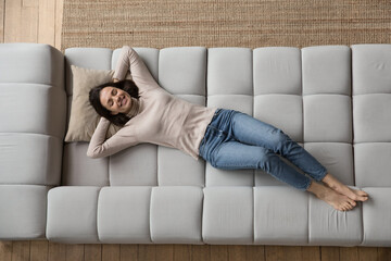 Relaxed cheerful beautiful 20s girl resting on soft comfortable big sofa, thinking, dreaming,...