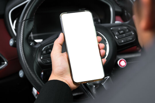 Close-up of woman's hands holding smartphone with empty space on screen for your text, background of car steering wheel. Mockup image blank screen cell phone.