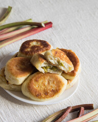 Fried pies with rhubarb on a plate on a light table, closeup. Delicious hot snack pirozhki.