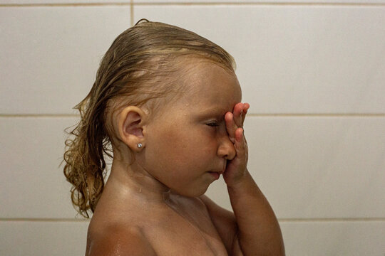 Child girl with closed eyes with wet hair takes a shower.