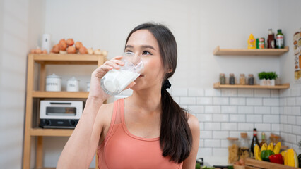 Asian Woman holding and drinking fresh milk from glass. healthy diet after exercise in kitchen,...