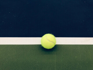 green tennis ball at the middle of the ending white line of tennis blue-green indoor court