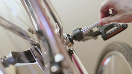 Man tightening metal bolts of connecting rod in bottom bracket assembly with socket wrench, close-up. Wheels of inverted bicycle are spinning. Mechanic checks technical condition of bike.