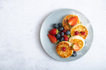 Fried cheesecakes on a plate with sour cream, berries and powdered sugar top view