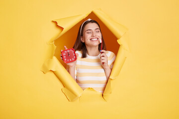 Beautiful satisfied woman wearing striped shirt and hair band, breaks through yellow paper...