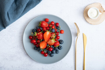 Strawberries, cherries and blueberries on a plate with a knife and fork, top view
