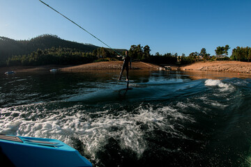 Athletic guy holds rope and riding with foil wakeboard on the river.