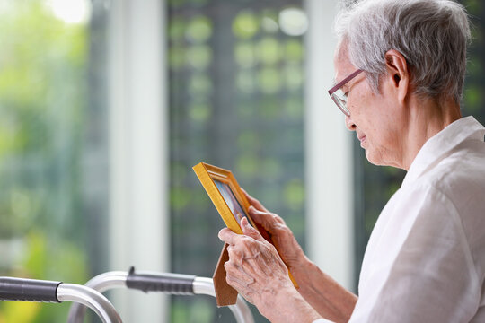 Sad old elderly with depression looks at photograph of her family with nostalgia,remembrance,Depressed asian senior woman patient holding picture frame,sitting alone in loneliness at nursing home