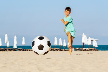 Football on beach. Boy soccer player kick ball trying to score goal in football match on sand....