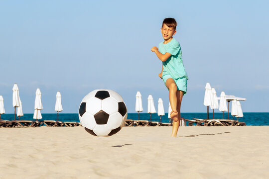 Football on beach. Boy soccer player kick ball trying to score goal in football match on sand. Active summer holiday outdoor on sea shore, sport, fun and enjoyment on vacation