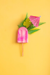 Pink ice cream with palm leaves and umbrella on a yellow background. Minimalist creative summer composition top view